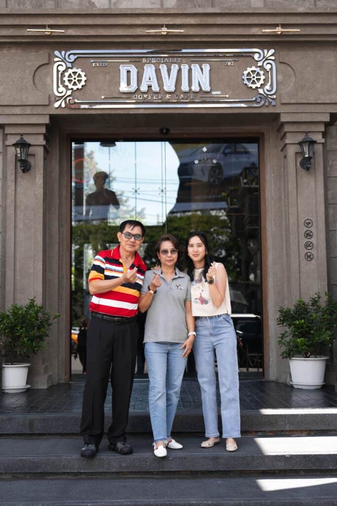 A family of three standing on the steps and posing for a photo in front of the Davin Cafe entrance.