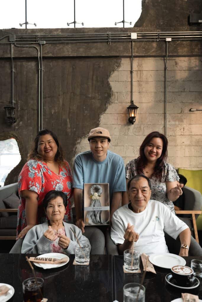 A happy family portrait, including parents and grandparents, celebrating a special occasion with a gift inside Davin Cafe.