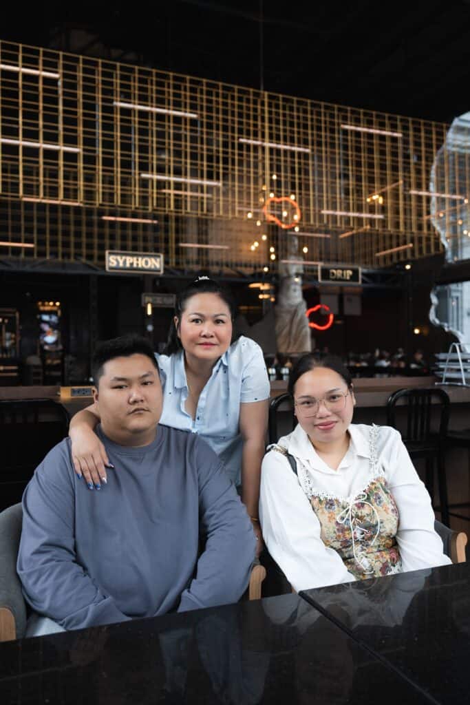 Three people sitting together inside Davin Cafe, with a golden grid structure and "Syphon" and "Drip" signs visible in the background.