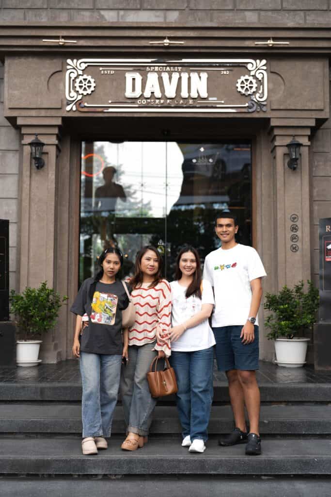 กลุ่มเพื่อนสี่คนกำลังยืนถ่ายรูปที่บันไดทางเข้าร้าน Davin Cafe.