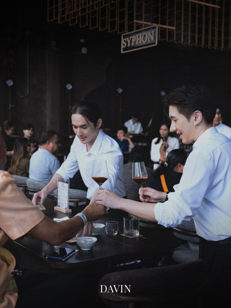 บาริสต้ากำลังเสิร์ฟกาแฟไซฟอนให้ลูกค้าที่โต๊ะภายในร้าน Davin Cafe.