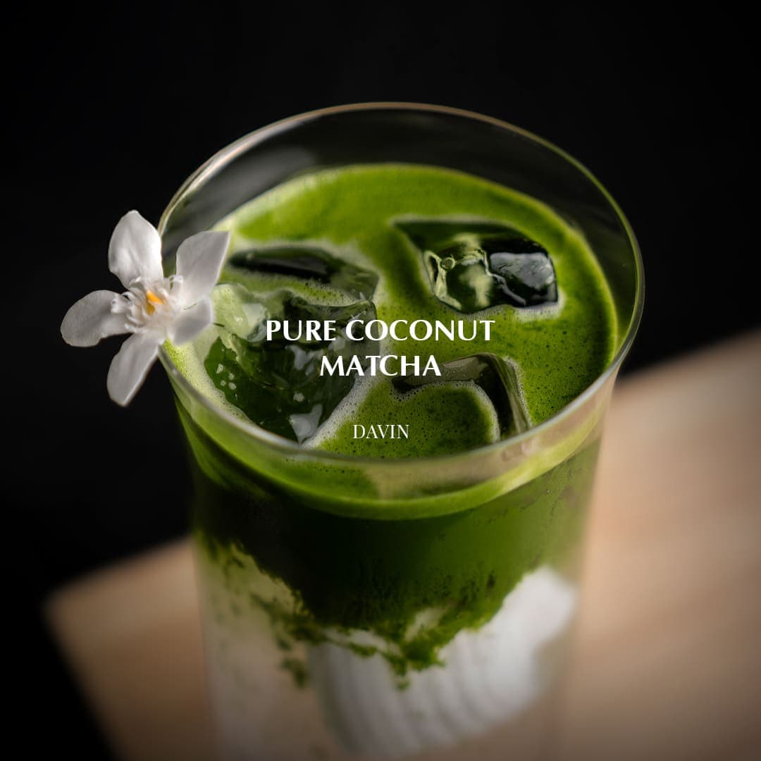 เครื่องดื่ม เพียวโคโคนัทมัทฉะ ของ Davin Cafe เสิร์ฟเย็นพร้อมน้ำแข็งและนมมะพร้าว ตกแต่งด้วยดอกไม้สีขาว.