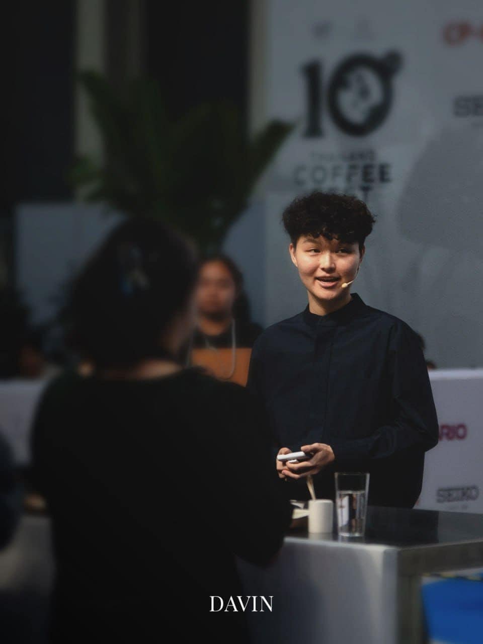 Coffee champion Jane Kawinnart smiling while speaking to an audience at a coffee event.