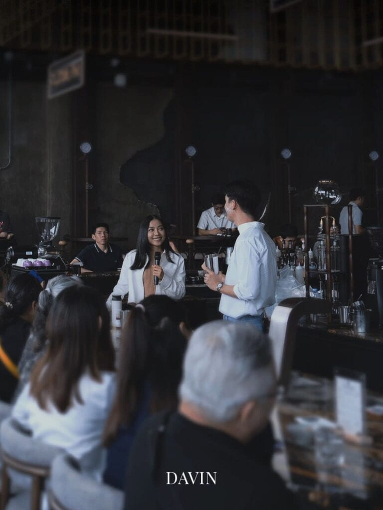 วิทยากรหญิงและชายกำลังนำเสนอและพูดคุยกับผู้ฟังภายในร้าน Davin Cafe.