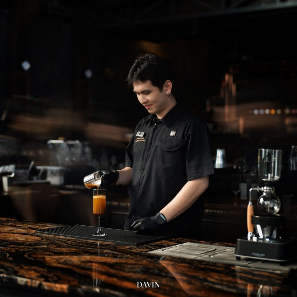 A Davin Cafe barista in uniform meticulously pouring ingredients to craft a signature mixed coffee drink at the marbled bar counter.