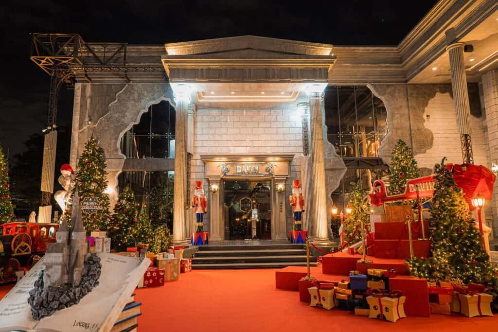The grand Christmas exterior of Davin Cafe at night, featuring a red carpet entrance flanked by illuminated Christmas trees, gift boxes, and large Nutcracker soldiers.