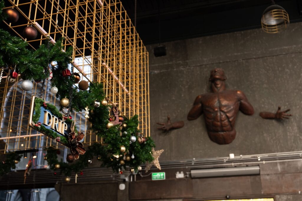 บรรยากาศภายในสถานที่จัดงานคริสต์มาส 2025 สไตล์อินดัสเทรียลอาร์ต ตกแต่งด้วยโครงสร้างโลหะสีทอง ประติมากรรมศิลปะ และพวงคริสต์มาส เหมาะสำหรับงานเลี้ยงคริสต์มาส งานฉลองปลายปี และอีเวนต์พรีเมียมที่ต้องการเอกลักษณ์ไม่ซ้ำใคร