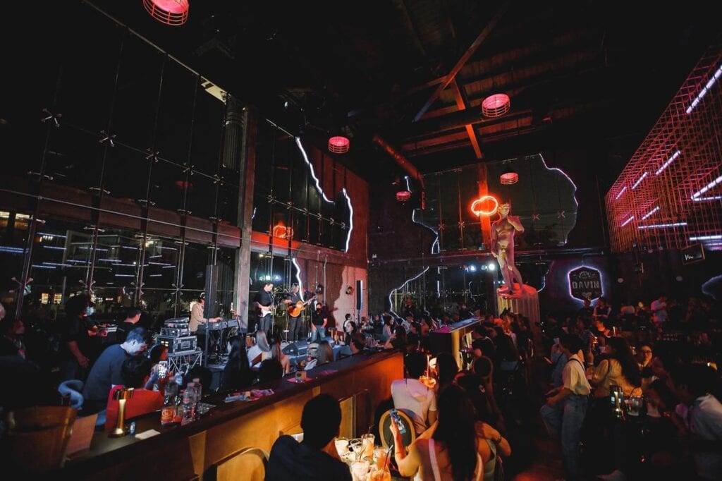 บรรยากาศสถานที่จัดปีใหม่ยามค่ำคืนภายในร้านอาหารและบาร์ที่มีดนตรีสด ผู้คนร่วมเฉลิมฉลองอย่างคึกคัก ท่ามกลางแสงไฟและการตกแต่งที่สร้างประสบการณ์งานเลี้ยงส่งท้ายปีสำหรับกลุ่มเพื่อนและองค์กรอย่างมีสไตล์