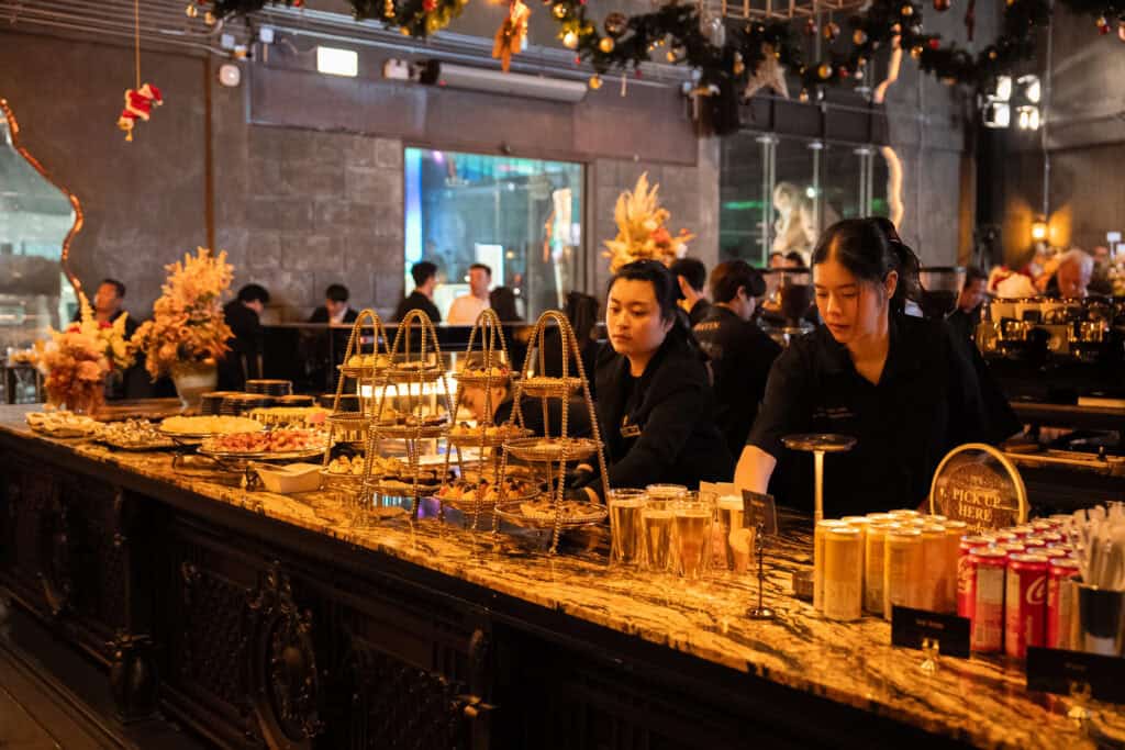 ทีมงานของร้านอาหารจัดเลี้ยงกำลังดูแลโซนอาหารและเครื่องดื่มในงานเลี้ยงบริษัท บริการอย่างเป็นระบบเพื่อรองรับแขกจำนวนมากตลอดงานอีเวนต์