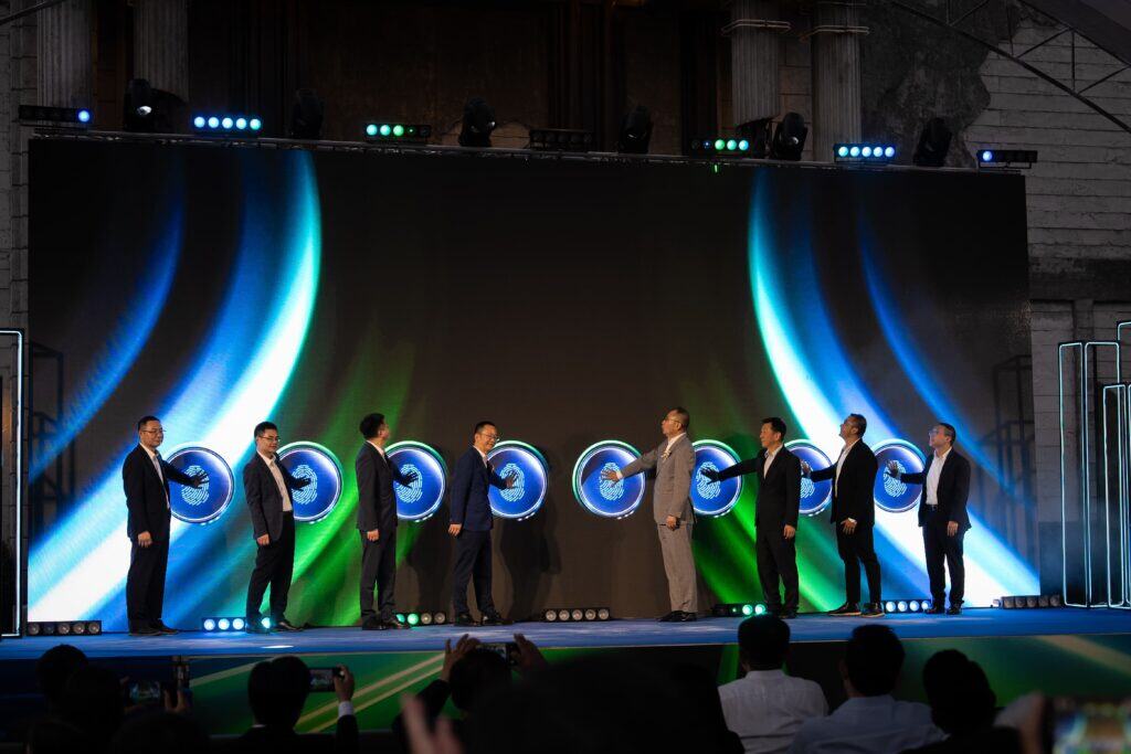 A professional event venue hosting a grand opening touch ceremony on a large LED stage with full lighting, production system, and corporate executives on stage