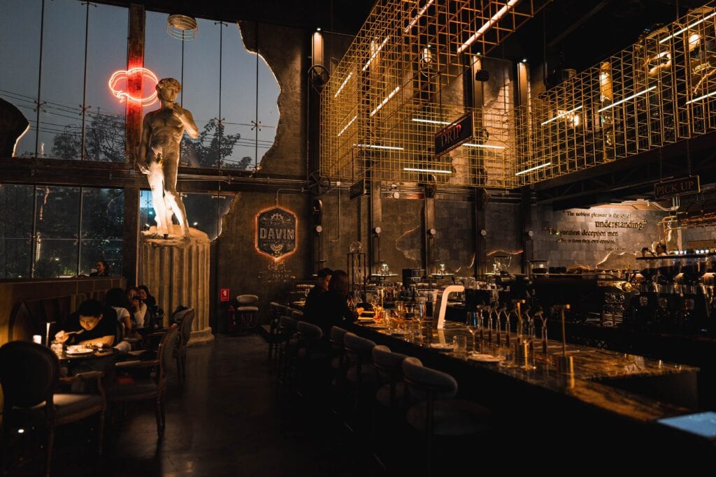 Industrial-style night hangout bar with a long counter, people relaxing, drinking, and socializing in a warm evening atmosphere