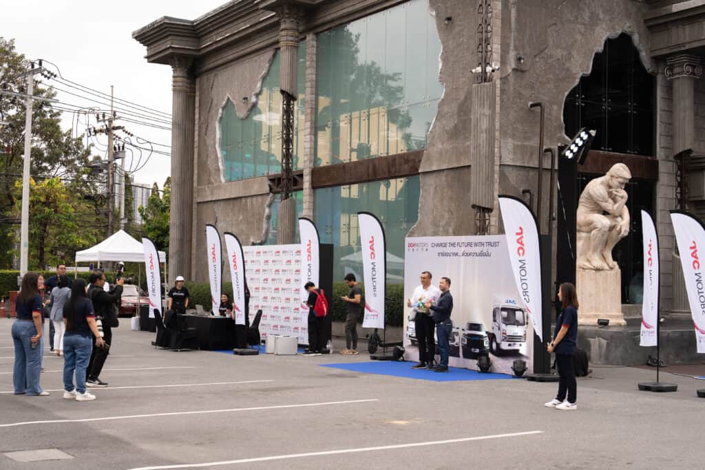 An outdoor event venue hosting a corporate brand activation with exhibition booths, staff, and real attendees in front of a distinctive architectural building