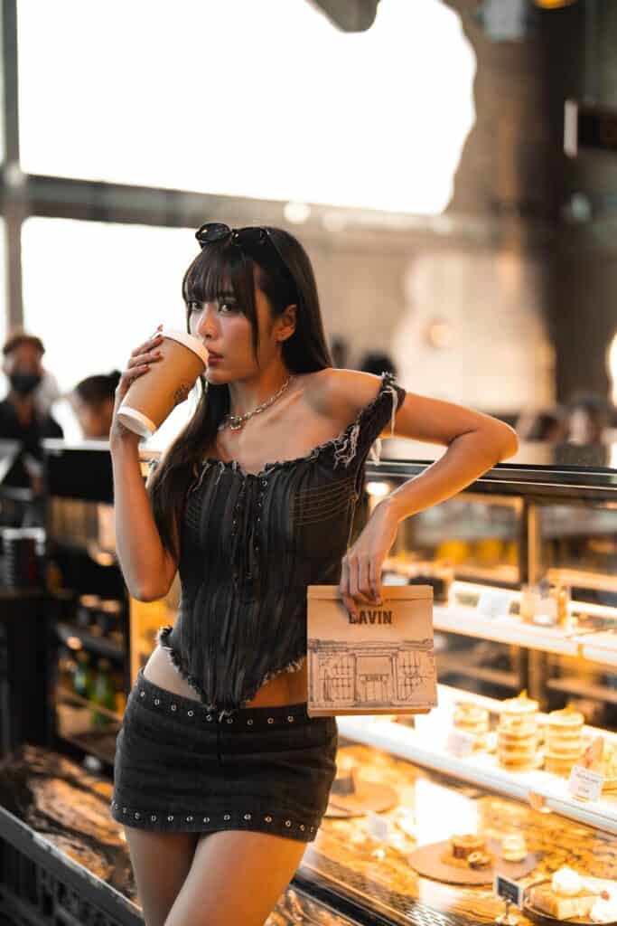 หญิงสาวกำลังดื่มกาแฟในคาเฟ่ถ่ายรูปสวย บรรยากาศอบอุ่น พร้อมมุมเบเกอรี่และไลฟ์สไตล์ที่เหมาะกับการถ่ายคอนเทนต์และคาเฟ่ฮอปปิ้ง