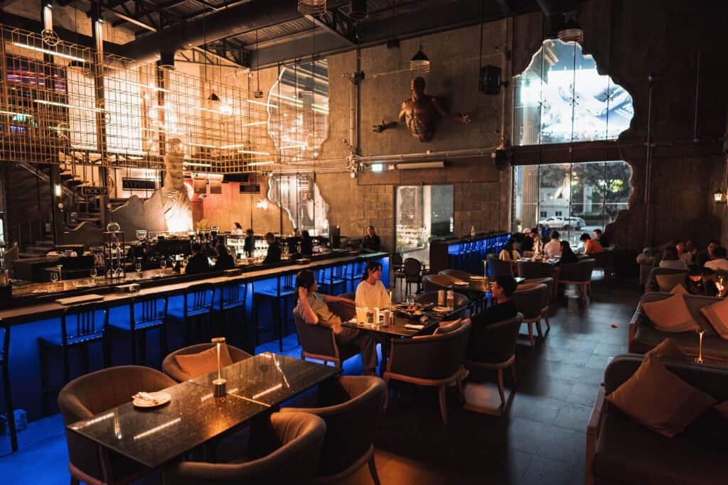 ร้านแฮงเอาต์บรรยากาศกลางคืน สไตล์อินดัสเทรียล มีทั้งเคาน์เตอร์บาร์และโต๊ะนั่ง ลูกค้านั่งดินเนอร์ พูดคุย และแฮงเอาต์ยามค่ำคืนอย่างเป็นส่วนตัว