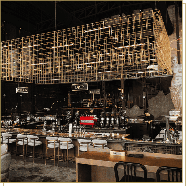 บรรยากาศโซนบาร์กาแฟขนาดใหญ่ของ Davin Cafe ที่ตกแต่งสไตล์ Steampunk ผสม Industrial Loft โดดเด่นด้วยกรงเหล็กสีทองและรูปปั้นกรีก พร้อมสเตชัน Slow Bar สำหรับ Drip และ Syphon ที่แสดงถึงความเชี่ยวชาญด้าน Specialty Coffee อย่างแท้จริง