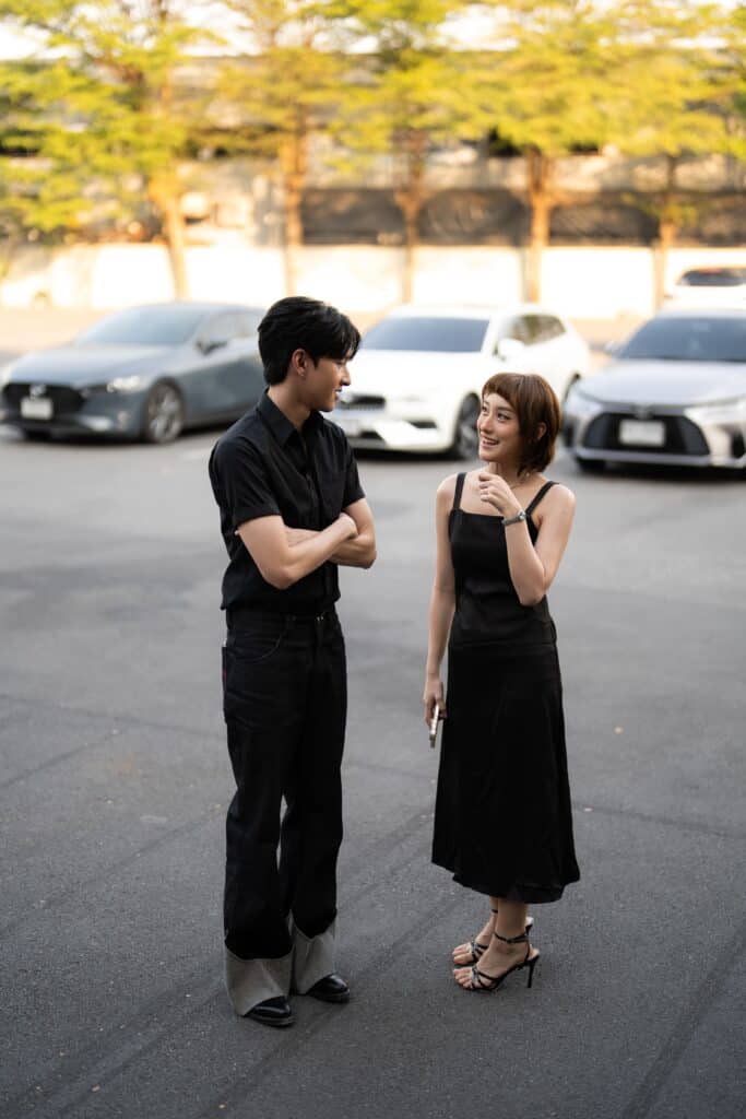 A stylish couple meeting for their first date in the evening, sharing a natural and slightly nervous moment before entering a romantic venue in Bangkok