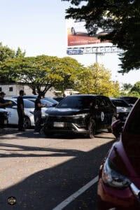 ที่จอดรถในงานอีเวนต์ The First Ultimate เที่ยวสุดโลก 15 พ.ย. 2025, มีรถยนต์หลายคันจอดอยู่ใต้ต้นไม้ใน.