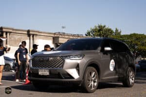 รถเอสยูวีสีเทาเข้มจอดในงานอีเวนต์พร้อมกลุ่มคนรอบข้างในบรรยากาศกลางแจ้ง.