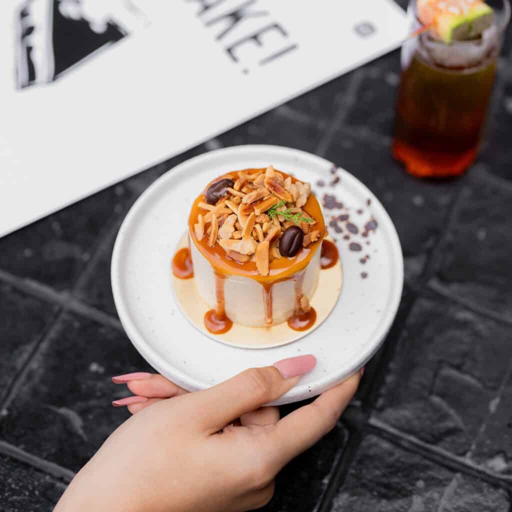 คาเฟ่เค้กอร่อย เมนู Almond Praline Coffee Cake เค้กกลิ่นกาแฟเข้มข้นท็อปด้วยอัลมอนด์กรุบกรอบและซอสคาราเมลในคาเฟ่ขนมหวานพรีเมียม
