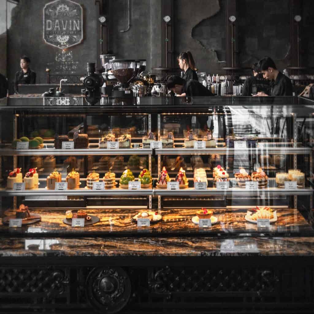 ตู้โชว์ขนมและเบเกอรี่ภายใน DAVIN CAFE คาเฟ่ เลียบด่วน ที่จัดเรียงอย่างสวยงาม พร้อมเมนูหลากหลายและบรรยากาศคาเฟ่สไตล์พรีเมียมที่ดึงดูดสายหวานและสายถ่ายรูป