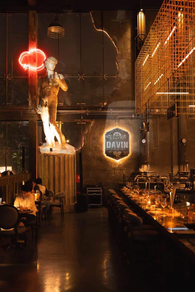 Luxury industrial interior at DAVIN CAFE featuring classical sculpture, warm ambient lighting, and stylish bar seating, a good atmosphere dinner spot perfect for upscale nighttime dining experiences