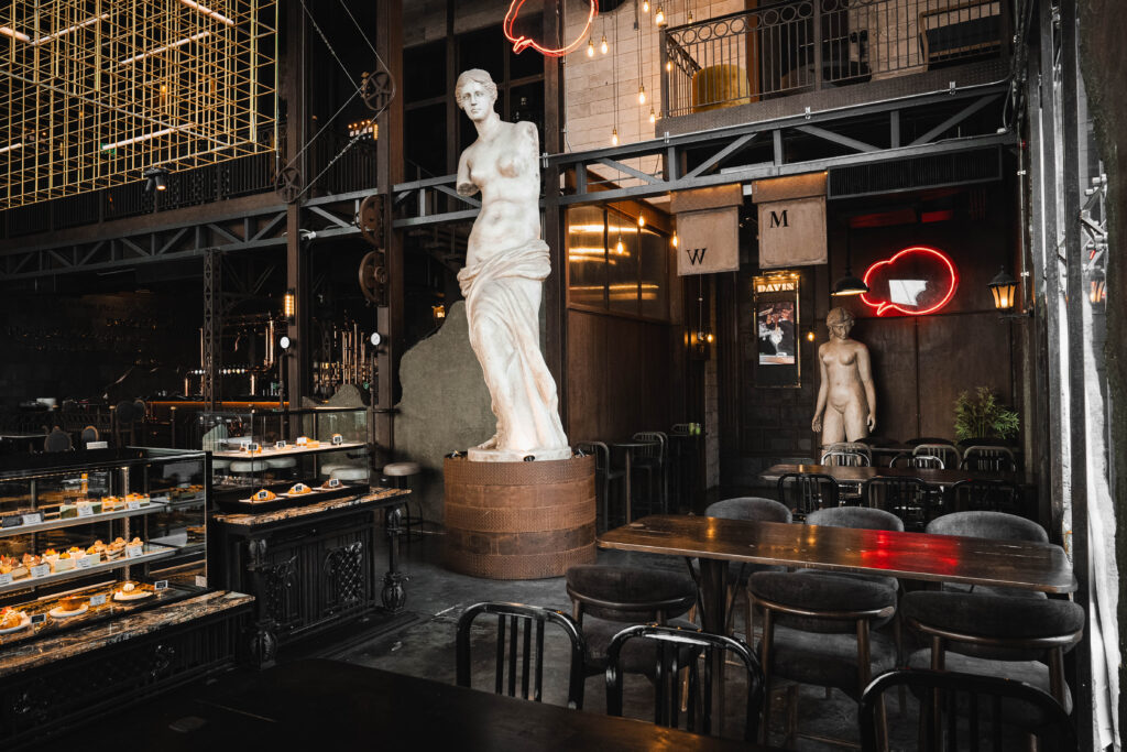 มุมที่นั่งภายใน Davin Cafe โทน Industrial Luxury พร้อมโต๊ะยาวและพื้นที่จัดเลี้ยง เหมาะสำหรับใช้เป็นสถานที่จัดสัมมนา กรุงเทพ แบบกลุ่มย่อยหรือประชุมทีมในบรรยากาศที่เป็นส่วนตัวและมีสไตล์