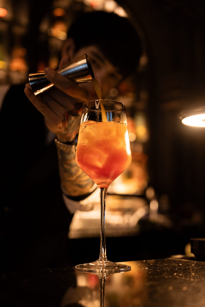 Skilled bartender crafting a signature cocktail at Vinsens, a stylish chill bar in Ramintra, highlighting mixology expertise, warm lighting, and a premium nightlife experience in Bangkok