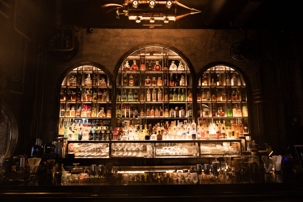 บาร์เครื่องดื่มภายในร้านอาหารจัดเลี้ยงและ cocktail bar ที่ตกแต่งด้วยชั้นสุราพรีเมียมและแสงอบอุ่น สร้างบรรยากาศหรูสำหรับค่ำคืนสุดพิเศษ