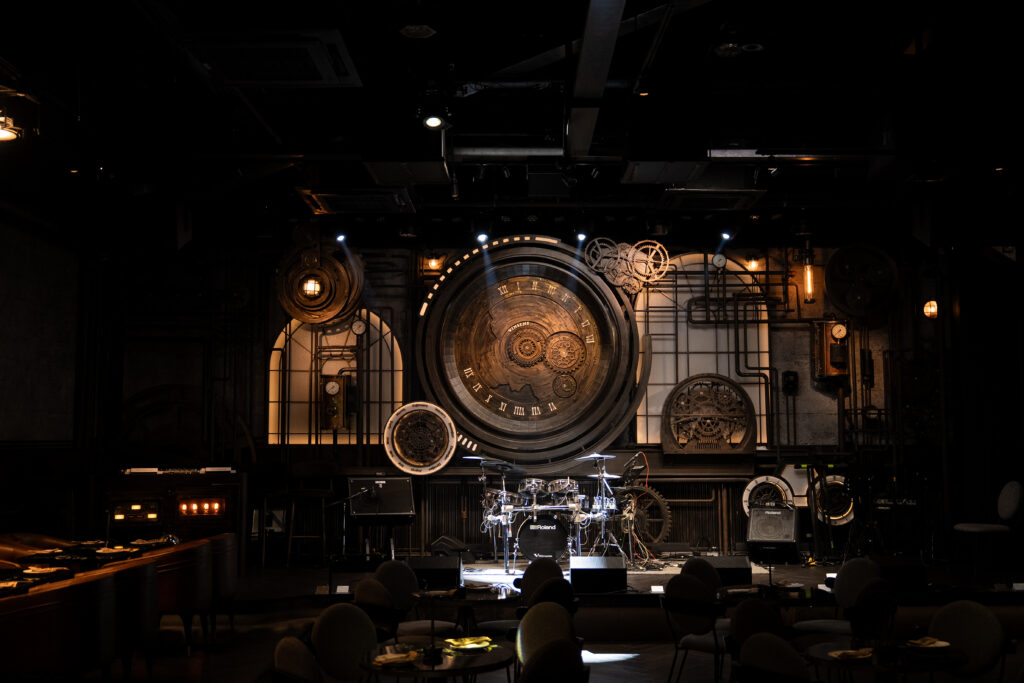 เวทีดนตรีสดภายในร้านอาหารจัดเลี้ยงและ cocktail bar สไตล์ Steampunk ของ Vinsens พร้อมดีไซน์นาฬิกาขนาดใหญ่ สร้างบรรยากาศพรีเมียมสำหรับคอนเสิร์ตและอีเวนต์ยามค่ำคืน