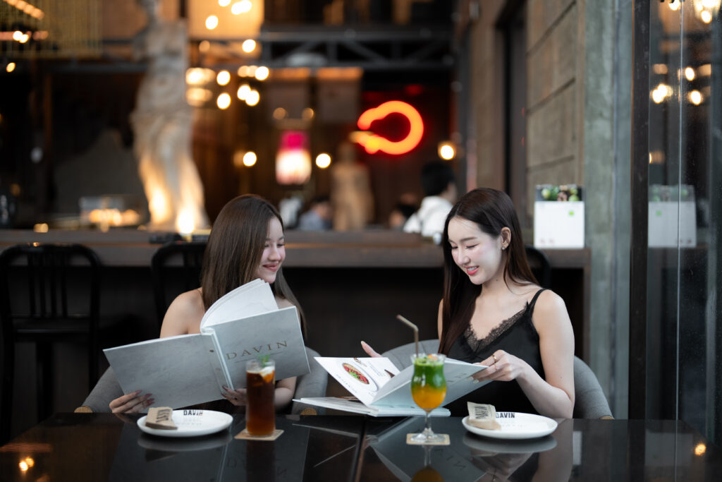 Guests browsing the menu with signature drinks inside Davin Cafe, a European-style cafe in Bangkok with elegant interiors, warm lighting, and a relaxed atmosphere for social coffee moments, dining, and photo-friendly cafe visits.