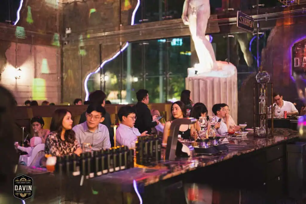 ผู้ร่วมงานนั่งพูดคุยและดื่มเครื่องดื่มบริเวณเคาน์เตอร์บาร์ของ Davin Cafe ท่ามกลางแสงสีและบรรยากาศพรีเมียม เหมาะสำหรับใช้เป็นสถานที่จัด Fan Meet ในกรุงเทพที่รองรับทั้งกิจกรรมพบปะแฟนคลับ ดินเนอร์กลุ่มเล็ก มุมถ่ายรูป และบริการอาหารเครื่องดื่มครบในที่เดียว