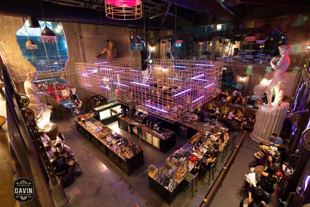 ภาพมุมสูงภายใน Davin Cafe ที่เห็นพื้นที่บาร์ขนาดใหญ่ โต๊ะนั่งหลายโซน แสงสี และดีไซน์ภายในที่โดดเด่น เหมาะสำหรับใช้เป็นสถานที่จัด Fan Meet ในกรุงเทพที่ต้องการพื้นที่รองรับผู้ร่วมงานจำนวนมาก กิจกรรมศิลปิน มินิคอนเสิร์ต มุมถ่ายรูป และบริการอาหารเครื่องดื่มครบในที่เดียว