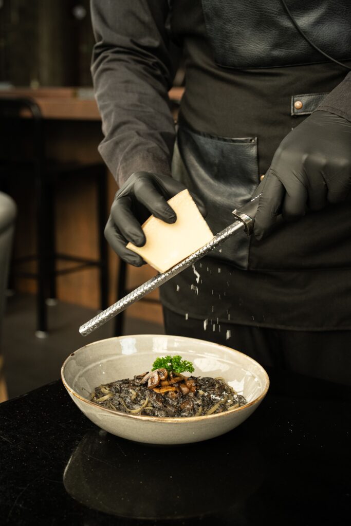 Chef finishing a signature black pasta dish with freshly grated cheese at DAVIN CAFE, a premium Liap Duan restaurant known for elevated dining and distinctive fine dining experiences
