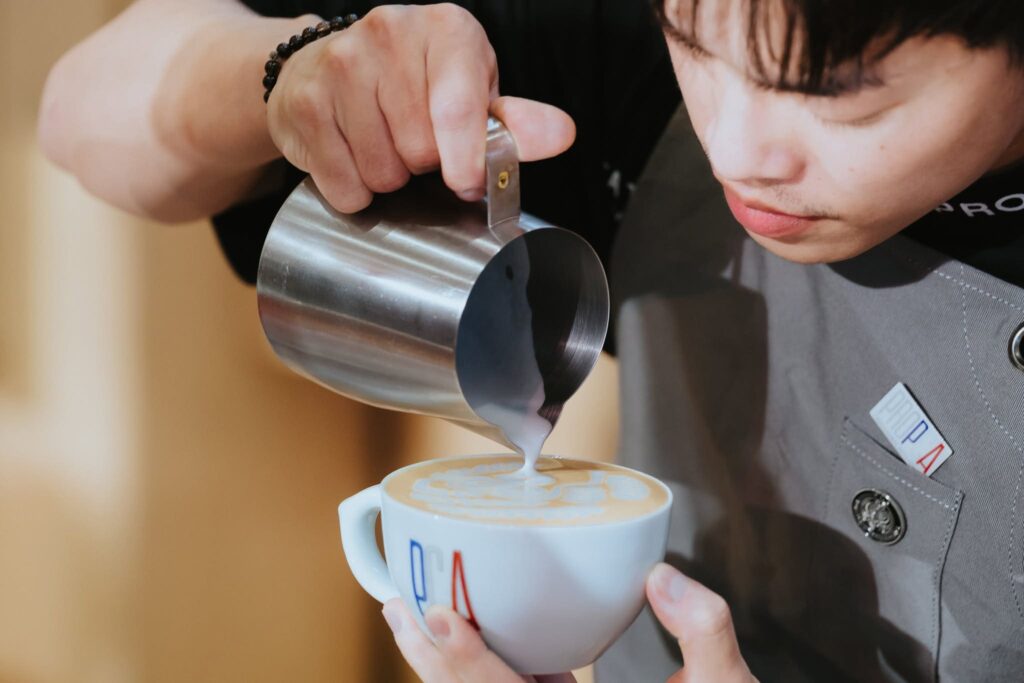 บาริสต้า DAVIN CAFE สาธิตเทคนิคการเทนมสร้างลวดลายลาเต้อาร์ตอย่างแม่นยำในรายการ PCA Latte Art Thailand 2026 สะท้อนความเชี่ยวชาญด้านกาแฟพิเศษและมาตรฐานการแข่งขันบาริสต้าระดับประเทศ