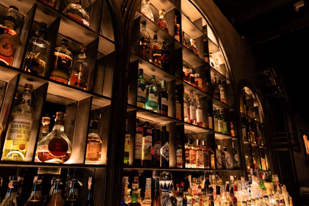Luxury liquor shelf inside VINSENS, a stylish chill bar in Bangkok with warm lighting, premium bottle displays, and a moody speakeasy atmosphere designed for cocktails, relaxed conversations, and refined nights out.