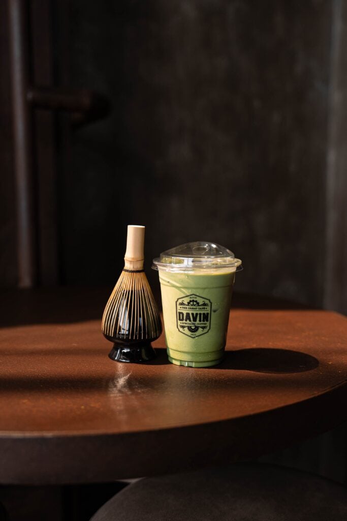 Premium Matcha Latte served at DAVIN CAFE Bangkok alongside a traditional Japanese bamboo whisk (Chasen), showcasing authentic ceremonial matcha craftsmanship with a smooth, creamy texture and rich green tea flavor.