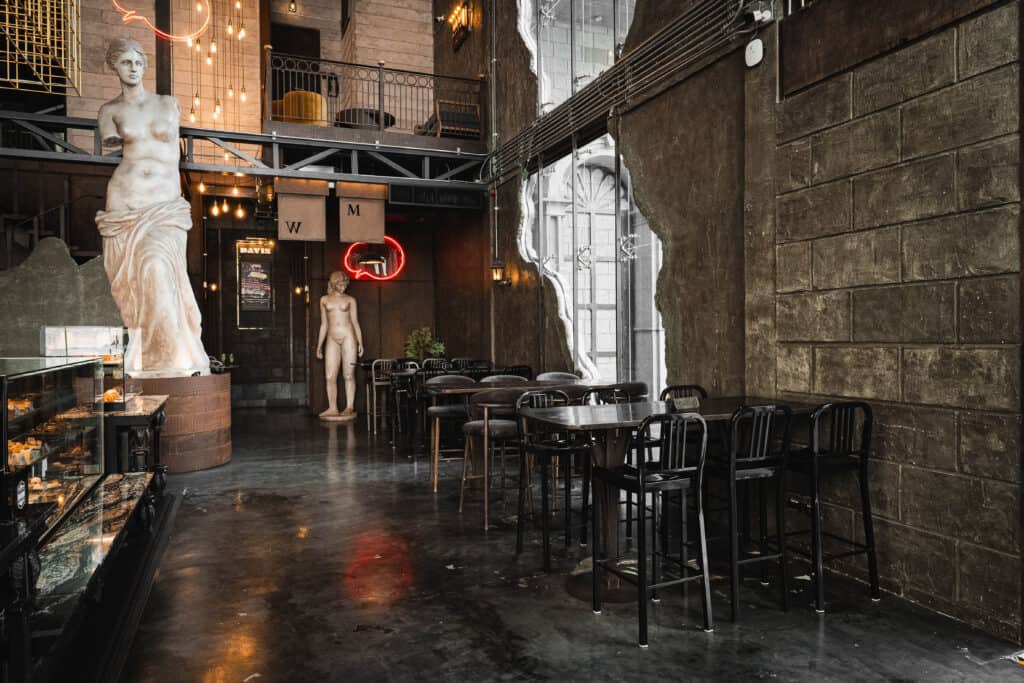 มุมที่นั่งภายใน Davin Cafe รามอินทรา ที่มีโต๊ะเก้าอี้จัดเป็นสัดส่วน เพดานสูง แสงธรรมชาติ และบรรยากาศสงบแบบยุโรป เหมาะสำหรับคนที่มองหาร้านกาแฟนั่งทำงานที่นั่งได้นาน มีความเป็นส่วนตัว และช่วยให้โฟกัสงานได้ดีระหว่างวัน