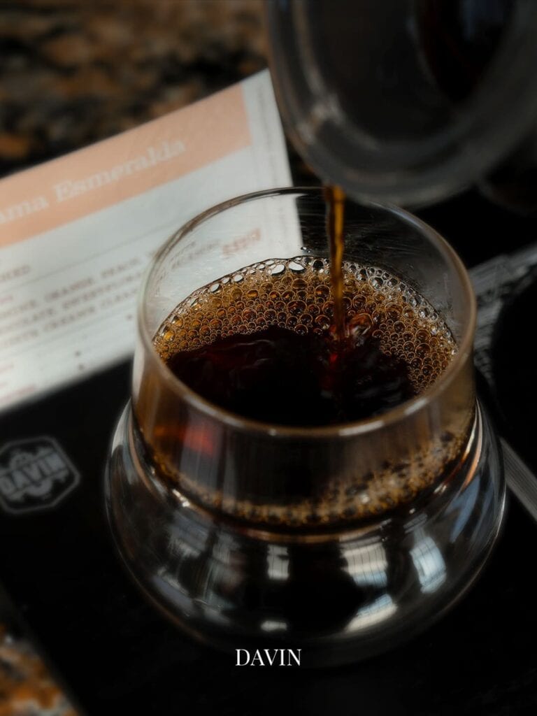 Pouring a carefully extracted specialty light roast coffee from a glass server, highlighting the clear and complex fruity tasting notes of the final brew.