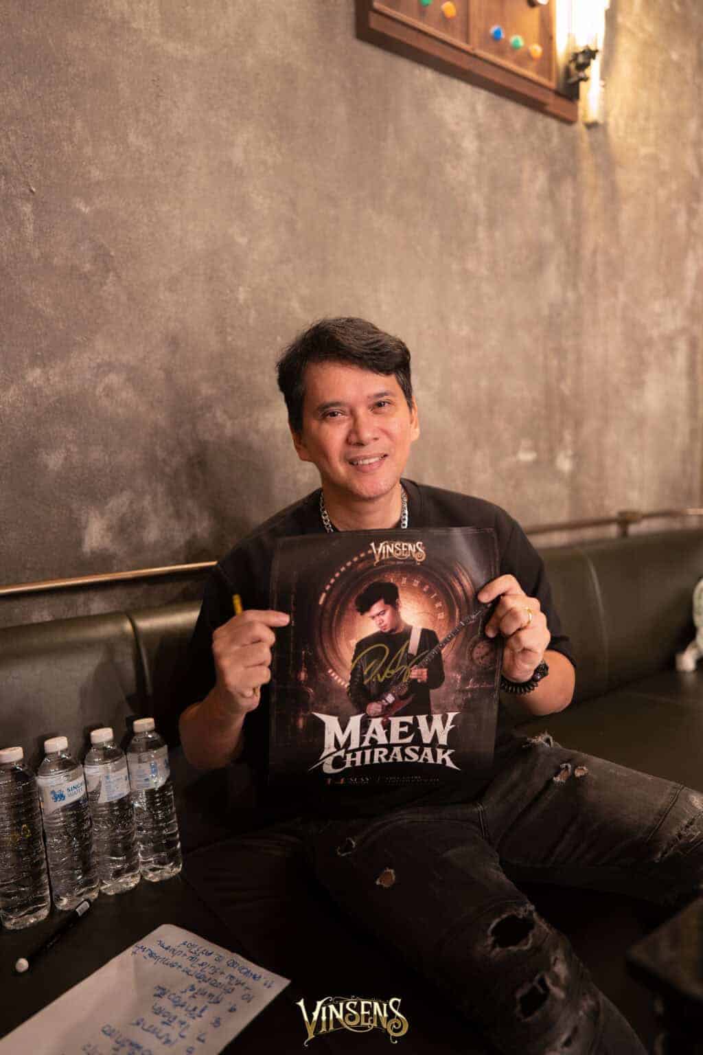 A renowned Thai rock artist holding his signed poster while relaxing at a premier fan meeting venue in Bangkok.