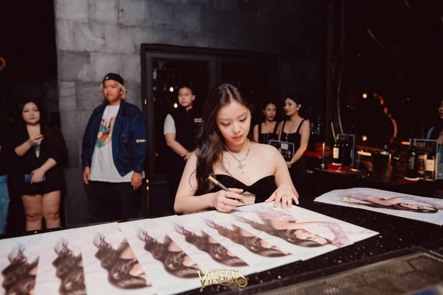 A famous celebrity elegantly signing posters for supporters at an exclusive fan meeting venue in Bangkok.