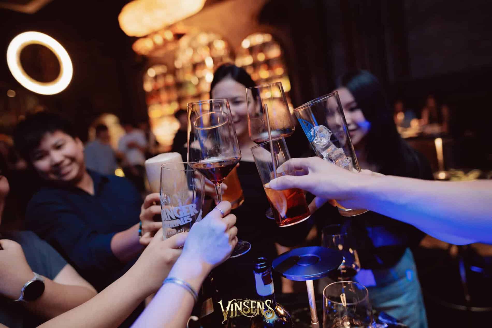 A group of excited fans clinking glasses and celebrating during a special event at a lively fan meeting venue in Bangkok.