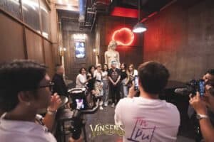A group of excited fans taking a memorable photo with an artist at a stylish fan meeting venue in Bangkok.