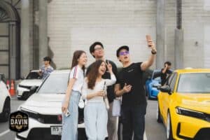 A group of friends taking a selfie next to a yellow sports car at a lively outdoor meetup space in Bangkok.