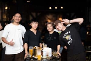 Friends smiling and posing for a photo with drinks at a lively party hosted in our indoor meetup space in Bangkok.