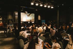 A large audience attentively watching a business presentation in the main hall of a seminar venue in Bangkok.