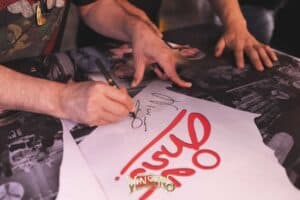 A close-up of a famous rock artist signing an autograph for a loyal fan at an intimate fan meeting venue in Bangkok.