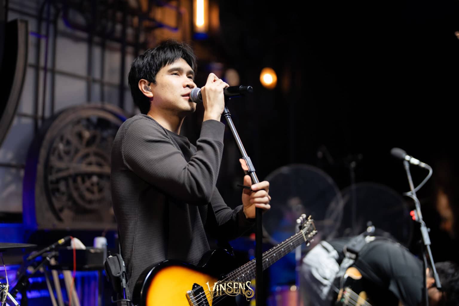 A talented male singer performing live on stage with a guitar at a popular fan meeting venue in Bangkok.