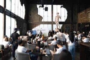 Wide shot of a corporate presentation with a speaker and seated attendees at a spacious, high-ceiling seminar venue in Bangkok.