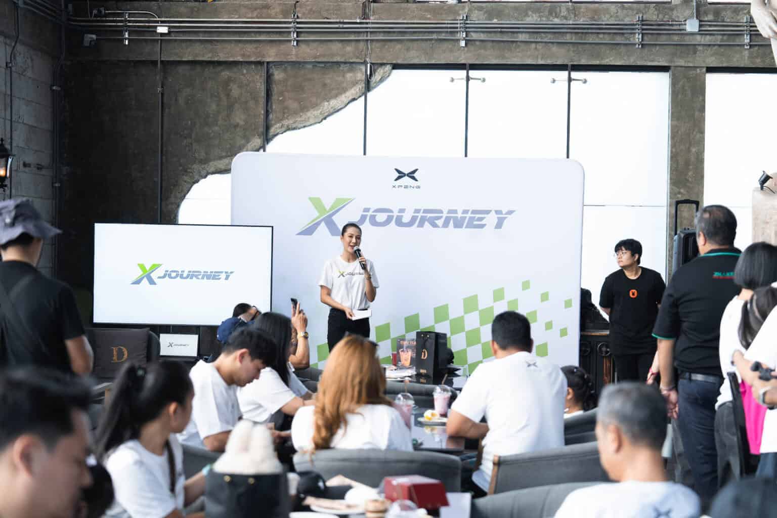 A female speaker giving a presentation on stage to a seated audience at a modern seminar venue in Bangkok.